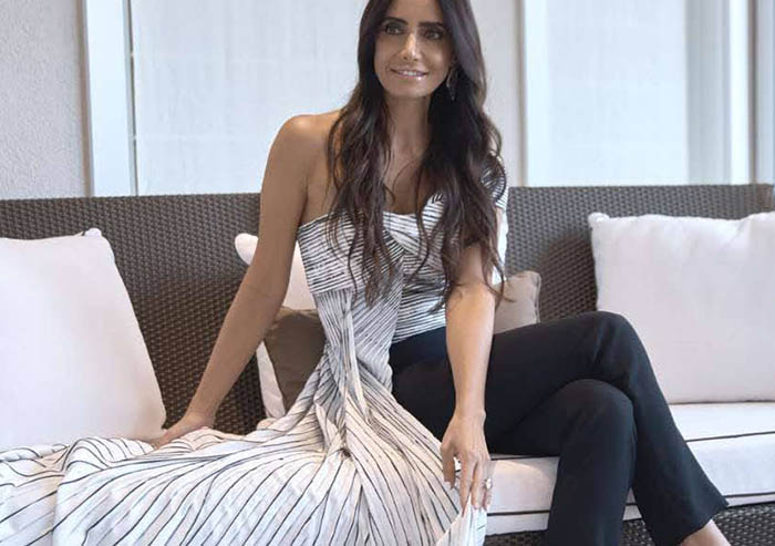 Abeer Al Otaiba displays the white and black striped fabric of her top while seated on a couch.